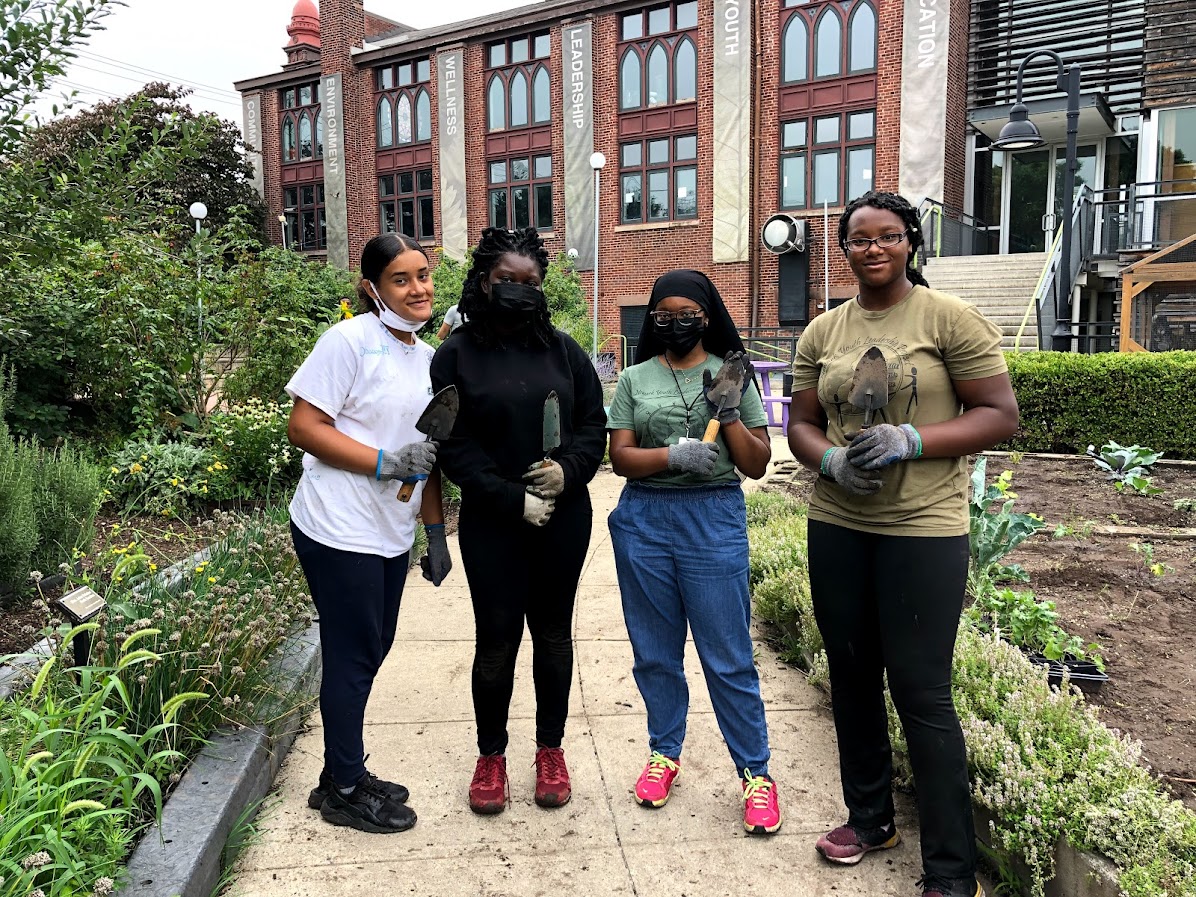 a group of teens stand in a garden with gardening tools